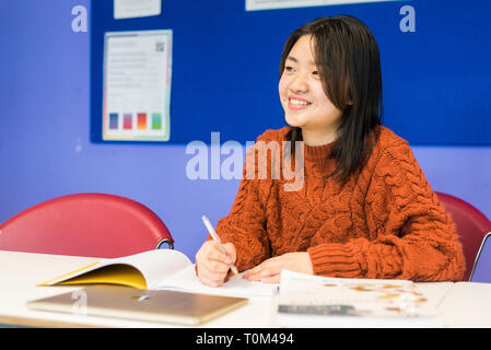 Un jeune étudiant asiatique est assis à un bureau dans une salle de classe à étudier au cours de sa leçon. Banque D'Images