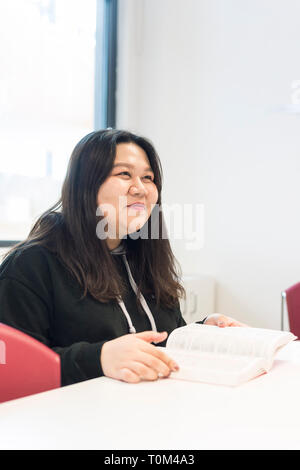 Un jeune étudiant asiatique est assis à un bureau dans une salle de classe à étudier au cours de sa leçon. Banque D'Images