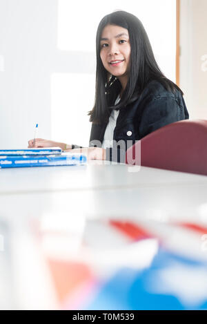 Un jeune étudiant asiatique est assis à un bureau dans une salle de classe à étudier au cours de sa leçon. Banque D'Images