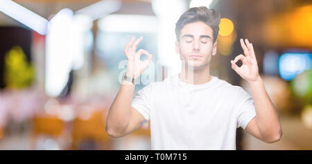 Beau jeune homme portant un t-shirt blanc sur fond isolé vous détendre et souriant avec les yeux fermé faisant le geste de la méditation avec les doigts. Conce Yoga Banque D'Images