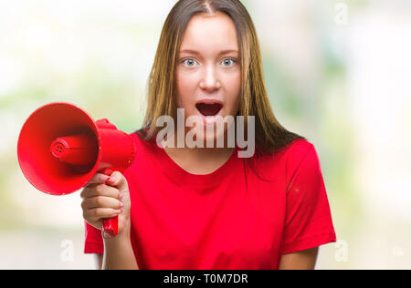 Young caucasian woman yelling through megaphone sur fond isolé en peur avec une surprise de Choc Visage, peur et excité par la peur d'expression Banque D'Images