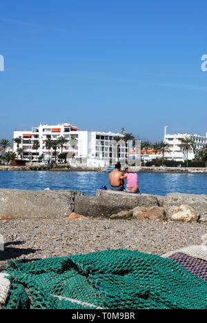 Filets de pêche sur le quai avec couple assis sur le bord du port face à la mer, Caleta de Velez, la province de Malaga, Andalousie, Espagne, Europe de l'Ouest. Banque D'Images