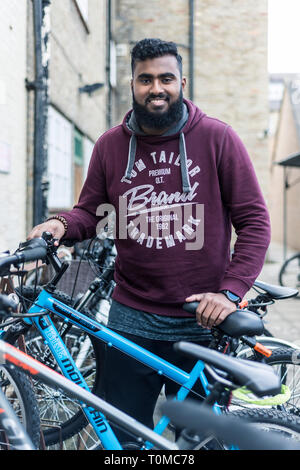 Un male international étudiant asiatique du sous continent, se dresse au milieu de la moto / stockage cycle dans un collège de Cambridge Banque D'Images