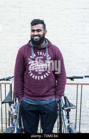 Un male international étudiant asiatique du sous continent, se dresse au milieu de la moto / stockage cycle dans un collège de Cambridge Banque D'Images