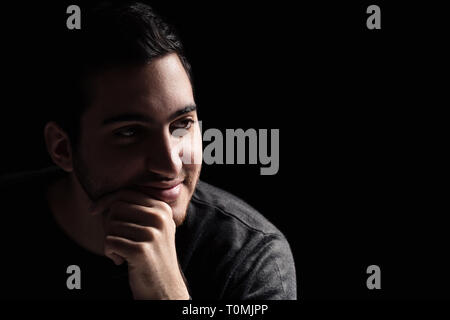 Portrait of a Young Man Thinking et souriant dans le noir Banque D'Images