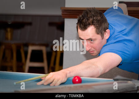 homme en t-shirt bleu visant un tir de piscine sur une table de bar dans un décor de pub public Banque D'Images