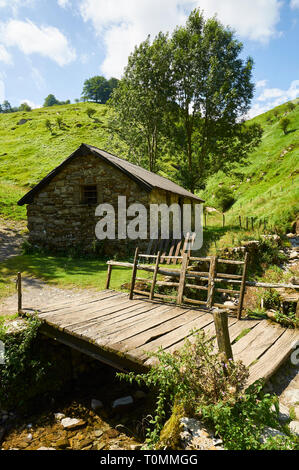 Chalet en pierre borda et pont en bois près de la grotte ARPEA, spectaculaire pli anticlinal entouré de pâturages verts dans les Pyrénées françaises (Estérençuby, France) Banque D'Images