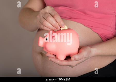 Les jeunes femmes enceintes entre 30 et 35 ans femme garde pink piggy bank. Libre Banque D'Images