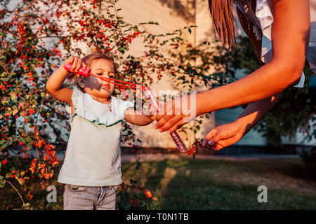 Petit bébé fille jouant avec des bulles de savon en parc d'été. Happy kid s'amusant à l'extérieur. Mother helping daughter. Activités d'été pour les enfants Banque D'Images