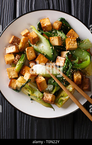 Tofu frit avec légumes asiatiques bok cho et sésame sur une assiette sur la table. Haut Vertical Vue de dessus Banque D'Images