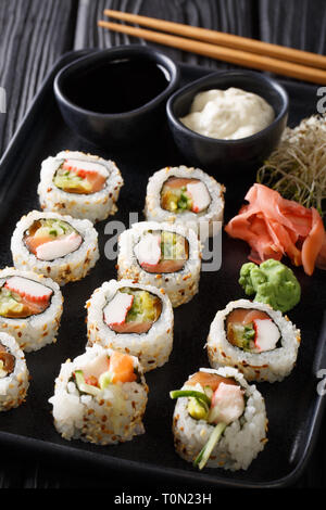 Rouleaux japonais frais servis avec des sauces, uramaki gingembre et wasabi libre sur une plaque sur la table verticale. Banque D'Images