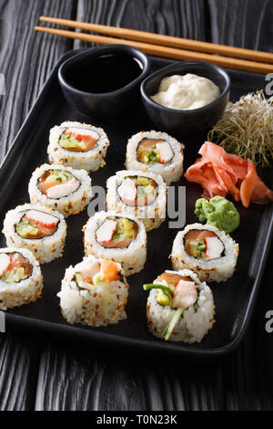 Rouleaux Uramaki sushi servi avec les sauces, le gingembre et le wasabi gros plan sur une plaque verticale sur la table. Banque D'Images