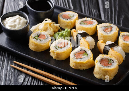 Les sushis japonais set roll avec du riz, de l'omelette, du fromage, du saumon et d'avocat servi avec des sauces, le wasabi et le gingembre sur une plaque sur la table horizontale. Banque D'Images