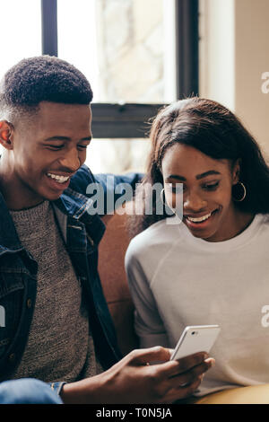 Étudiants adolescents assis ensemble dans la construction du campus à l'aide de smart phone. Garçon et fille assis à canapé looking at mobile phone et souriant. Banque D'Images