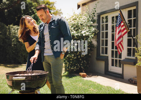 Smiling man and woman cooking dans son jardin avec le drapeau américain en arrière-plan. Couple grillades célébration d'une occasion. Banque D'Images