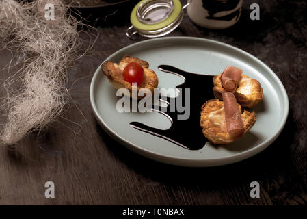 Photo horizontale de la plaque bleue avec Puff Pastry cups. Tasses sont farcies de fromage fondu. Le jambon et les tomates sont rouges sur des pâtisseries fraîches. Spi est la sauce sombre Banque D'Images