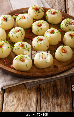 Boulettes de pommes de terre traditionnelle de Silésie avec bacon et oignons verts gros plan sur une plaque verticale sur la table. Banque D'Images