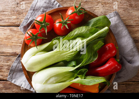 Bébé en santé matières premières le bok choy, tomates et poivrons libre sur une plaque sur une table en bois. Haut horizontale Vue de dessus Banque D'Images