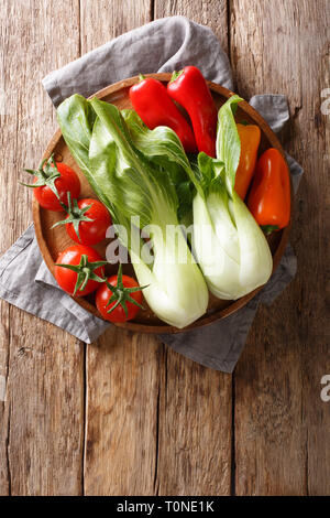 Des ingrédients frais petits bok choy, les tomates et les poivrons sur une plaque sur une table en bois. Haut Vertical Vue de dessus Banque D'Images