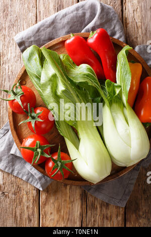 Bébé en santé matières premières le bok choy, tomates et poivrons libre sur une plaque sur une table en bois. Haut Vertical Vue de dessus Banque D'Images