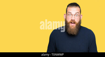 Jeune homme portant des lunettes et Pull col roulé de peur et choqué avec l'expression de surprise, la peur et excité face. Banque D'Images