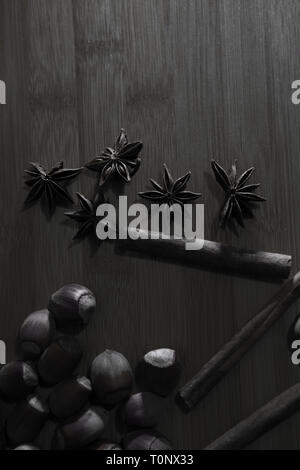 L'anis étoilé, de noisettes et de la cannelle sur planche de bois clé faible en noir et blanc Banque D'Images