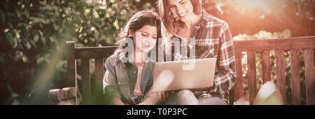 Smiling mother and daughter using laptop while sitting on banc en bois Banque D'Images