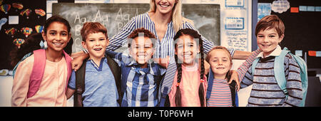 Happy teacher standing avec schoolkids in classroom Banque D'Images