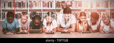 Enfants et enseignants lying on floor using digital tablet in library Banque D'Images