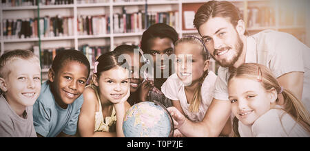 Les élèves et l'enseignant looking at globe in library Banque D'Images