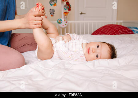 Portrait of cute adorable race mixte bébé asiatique lying on bed sur son dos. Mère de faire des massages et des exercices physiques pour nouveau-né. Développement précoce Banque D'Images