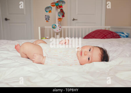 Portrait of cute adorable Asian mixed race baby girl 4 mois allongée sur le dos sur le lit dans la chambre. La diversité de la petite enfance vie candide Banque D'Images