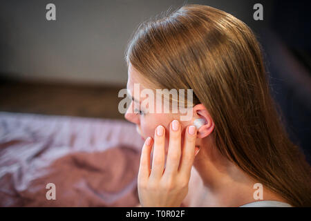 Photo de jeune femme assise sur le lit. Elle détient la main près de l'oreille. Elle fait sur elle. Il est fermé avec morceau de coton. Personne de sexe féminin souffre de Banque D'Images