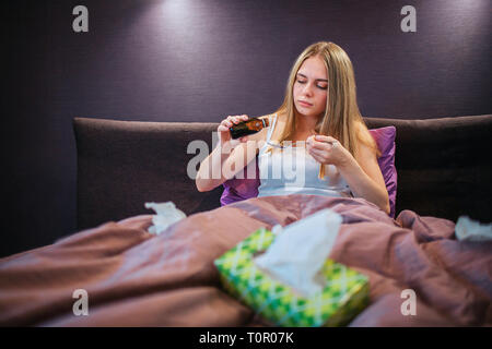 Belle jeune femme est assise sur le lit et poures certains traitements sur la cuillère. Elle est concnetrated sur cela. Il y a des zone verte de tissus blanc sur lit et Banque D'Images