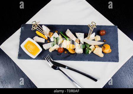 Plateau de fromages assortiment de différents types de fromage sur ardoise foncé planche à découper. Le Camembert, rococo, le parmesan, les noix, les tomates cerises, le mandarin, l'o Banque D'Images