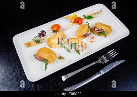 Mousse au fromage avec du bacon dans eclair, servi sur une assiette et couverts de vert et de tomate cherry Banque D'Images