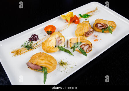 Mousse au fromage avec du bacon dans eclair, servi sur une assiette et couverts de vert et de tomate cherry Banque D'Images