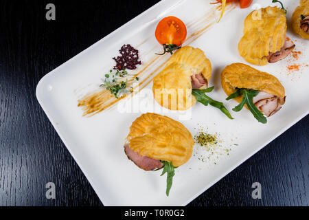 Mousse au fromage avec du bacon dans eclair, servi sur une assiette et couverts de vert et de tomate cherry Banque D'Images