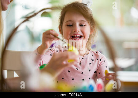 Une mère et sa fille célébrer Pâques, œufs de peinture avec pinceau. Cute little girl in Bunny Ears préparer les vacances. Banque D'Images