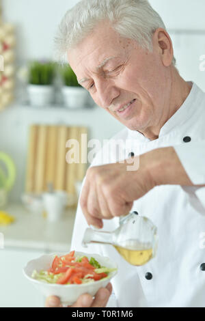 Close-up portrait of elderly male chef versez de l'huile dans la salade Banque D'Images