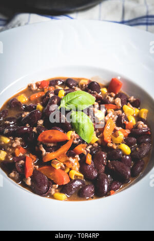 Chili ou de maïs chili carne. Haricots cuits, la viande hachée, le piment, le maïs et le poivre dans un bol blanc sur noir table de pierre Banque D'Images