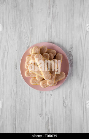 Savoyardi ou biscuits biscuits cookies sur la plaque en bois blanc, rose sur la surface, vue du dessus. Mise à plat, les frais généraux, d'en haut. Banque D'Images