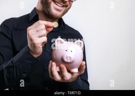 Young man putting coins in piggy bank. Épargner pour un jour de pluie Banque D'Images