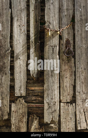 Une vieille chaîne rouillée, avec un cadenas sur une planche en bois branlant au fil des ans de porte Banque D'Images