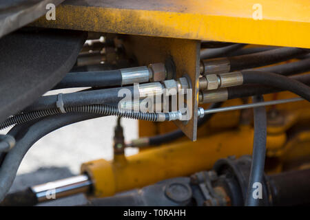 Système hydraulique connexions flexibles et tachée de bitume détails de machines routières jaune gros plan sur un arrière-plan flou d'autres mécanismes et équiper Banque D'Images