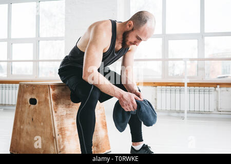 Assez musclé homme assis sur fort dans la salle de sport. Athlète masculin solide se reposant après entraînement intensif Banque D'Images