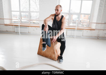 Assez musclé homme assis sur fort dans la salle de sport. Athlète masculin solide se reposant après entraînement intensif Banque D'Images