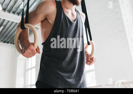 Anneaux de gymnastique athlète masculin tenant à la salle de sport. L'homme est remise en forme accroché sur les anneaux de gymnastique en salle de sport Banque D'Images