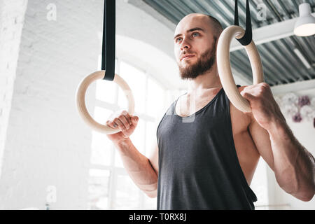 Anneaux de gymnastique athlète masculin tenant à la salle de sport. L'homme est remise en forme accroché sur les anneaux de gymnastique en salle de sport Banque D'Images