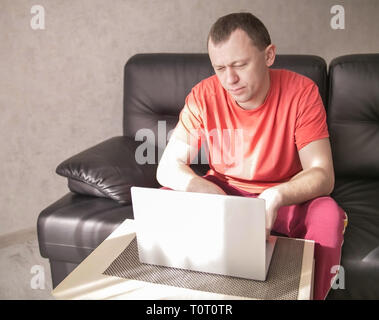 Jeune homme sérieux assis près de un ordinateur portable dans son salon sur un après-midi ensoleillé, copyspace Banque D'Images